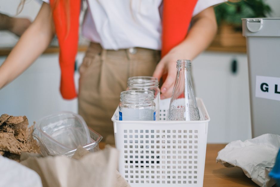 Crop anonymous female in casual clothes sorting out rubbish and selecting glass into container in kitchen