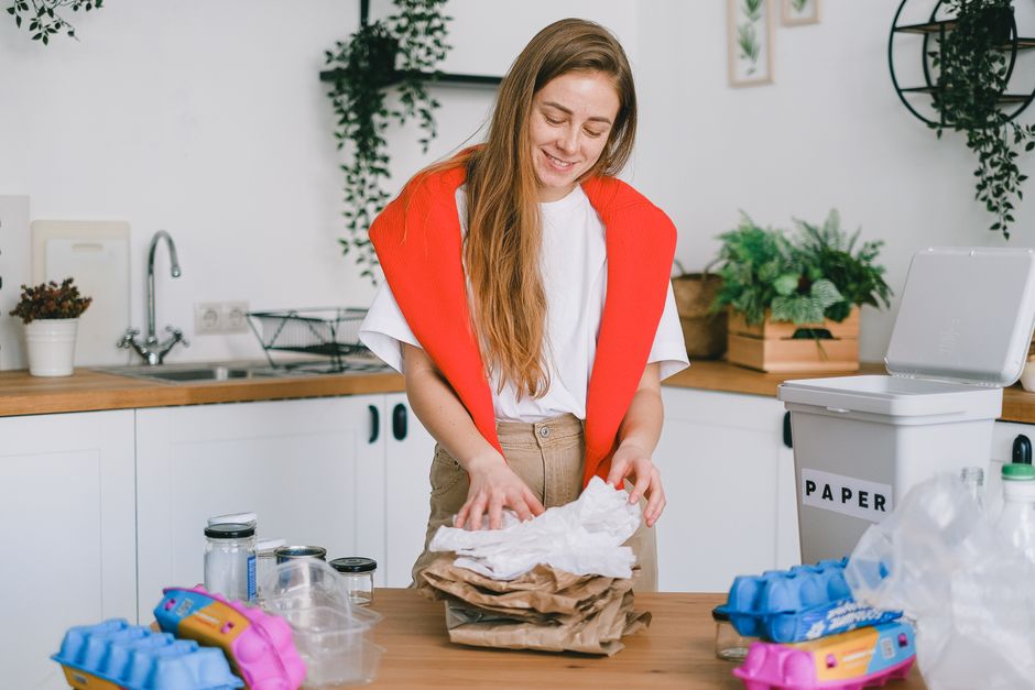 Positive female standing at table and separating paper trash from plastic glass and egg boxes