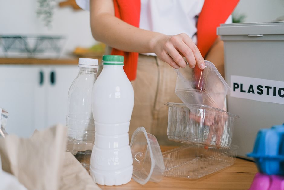 Crop anonymous female in casual clothes sorting out plastic containers and bottles into rubbish bin in kitchen
